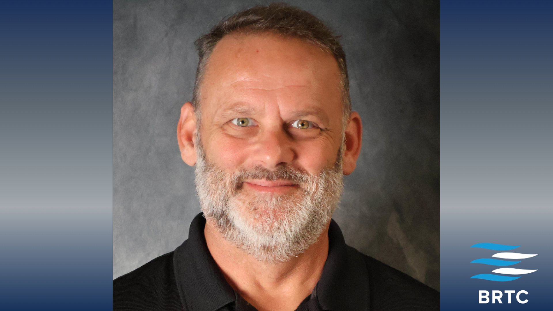A man with short gray hair and a full gray beard, wearing a black polo shirt, smiles in a professional headshot against a gray background, with the BRTC logo.